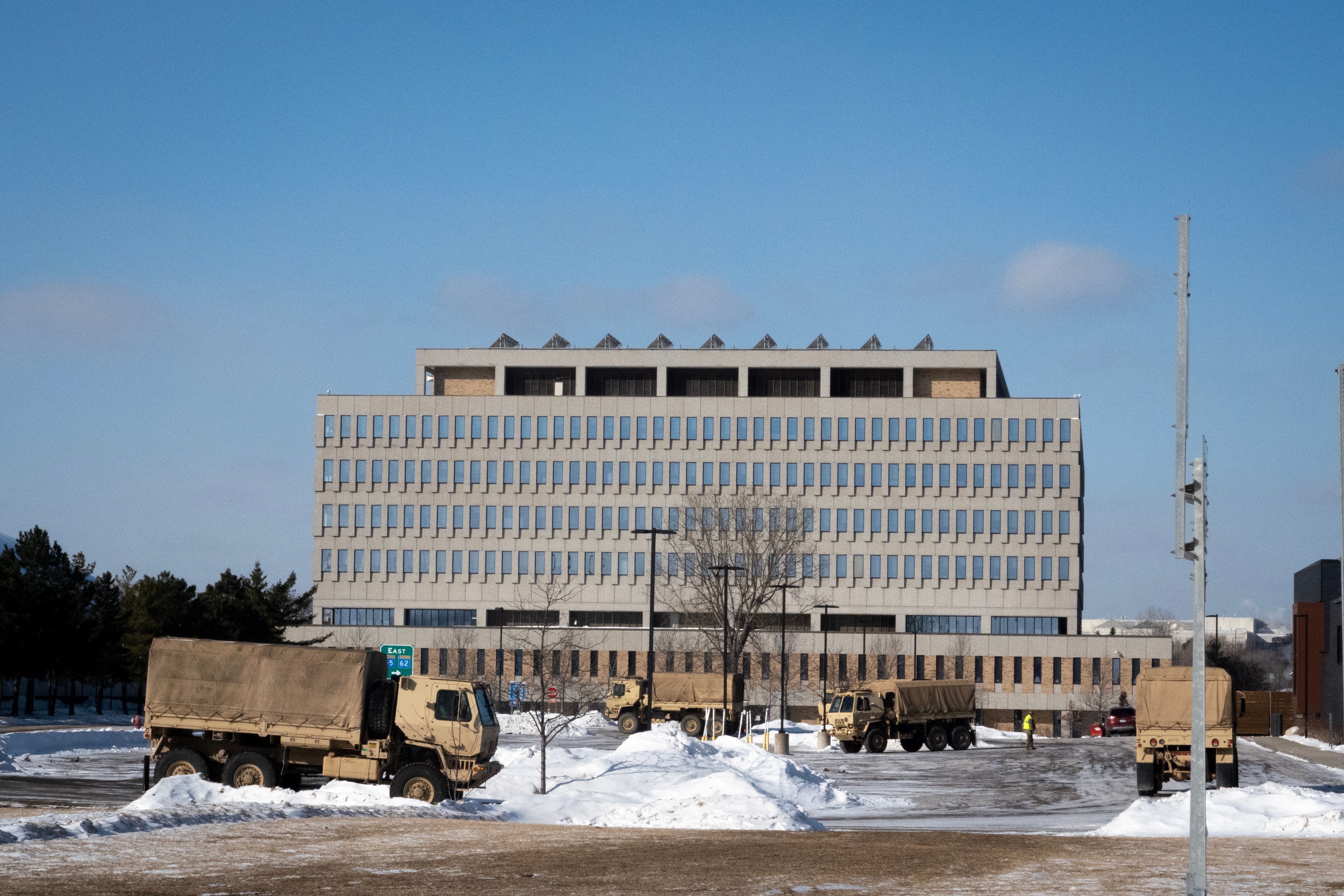Militære lastebiler parkert utenfor en stor regjeringsbygning i flere etasjer i et snølandskap