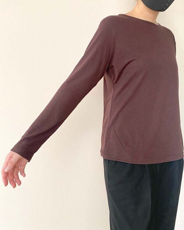 UNIQLO（ユニクロ）の「シアーT」黒のパンツとシンプルな長袖シャツを着た女性が片腕を伸ばして立っている。