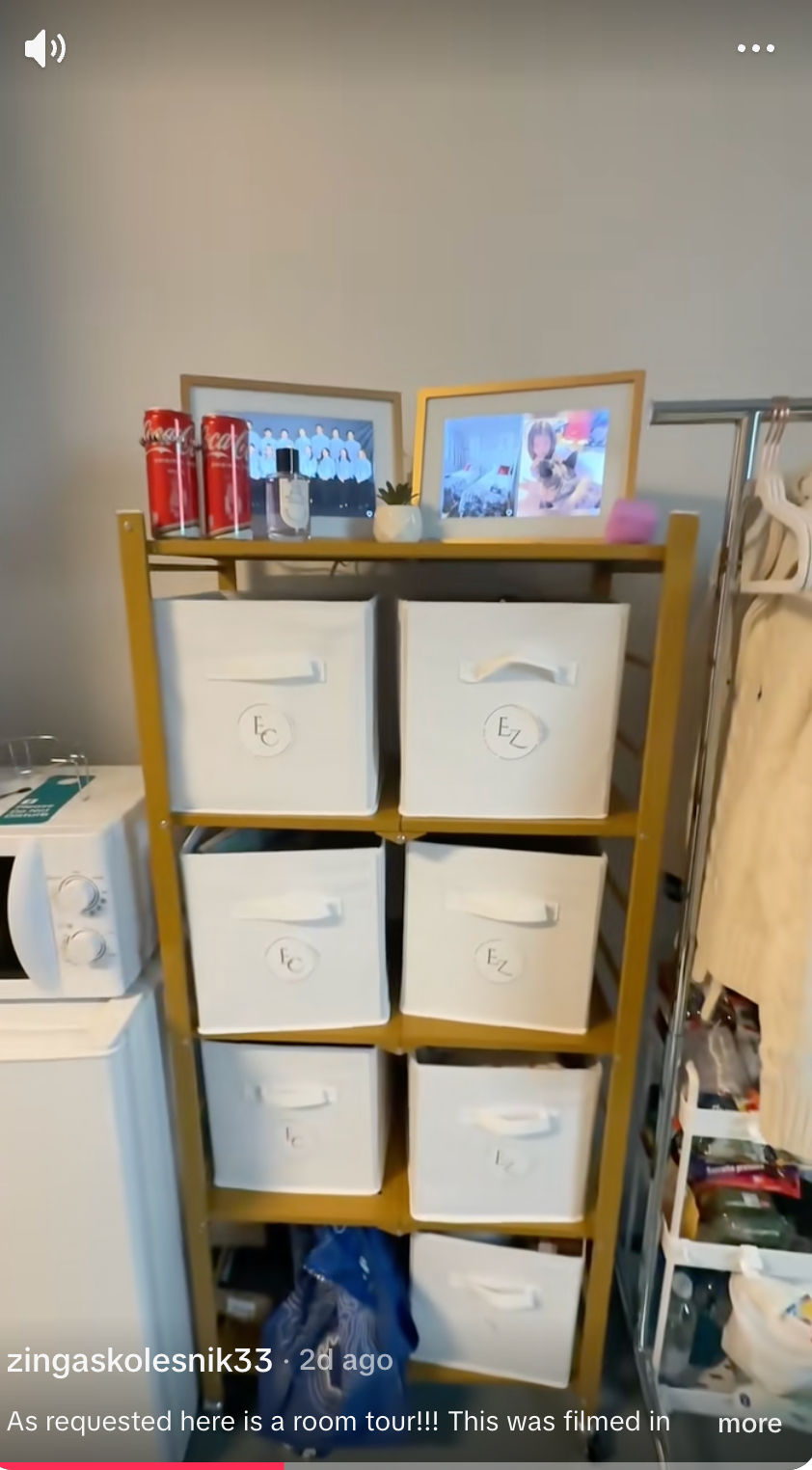 Room with retention  support  containing bins and a fewer  soda cans connected  top. A photograph  framework  and microwave are visible, with apparel  hanging nearby