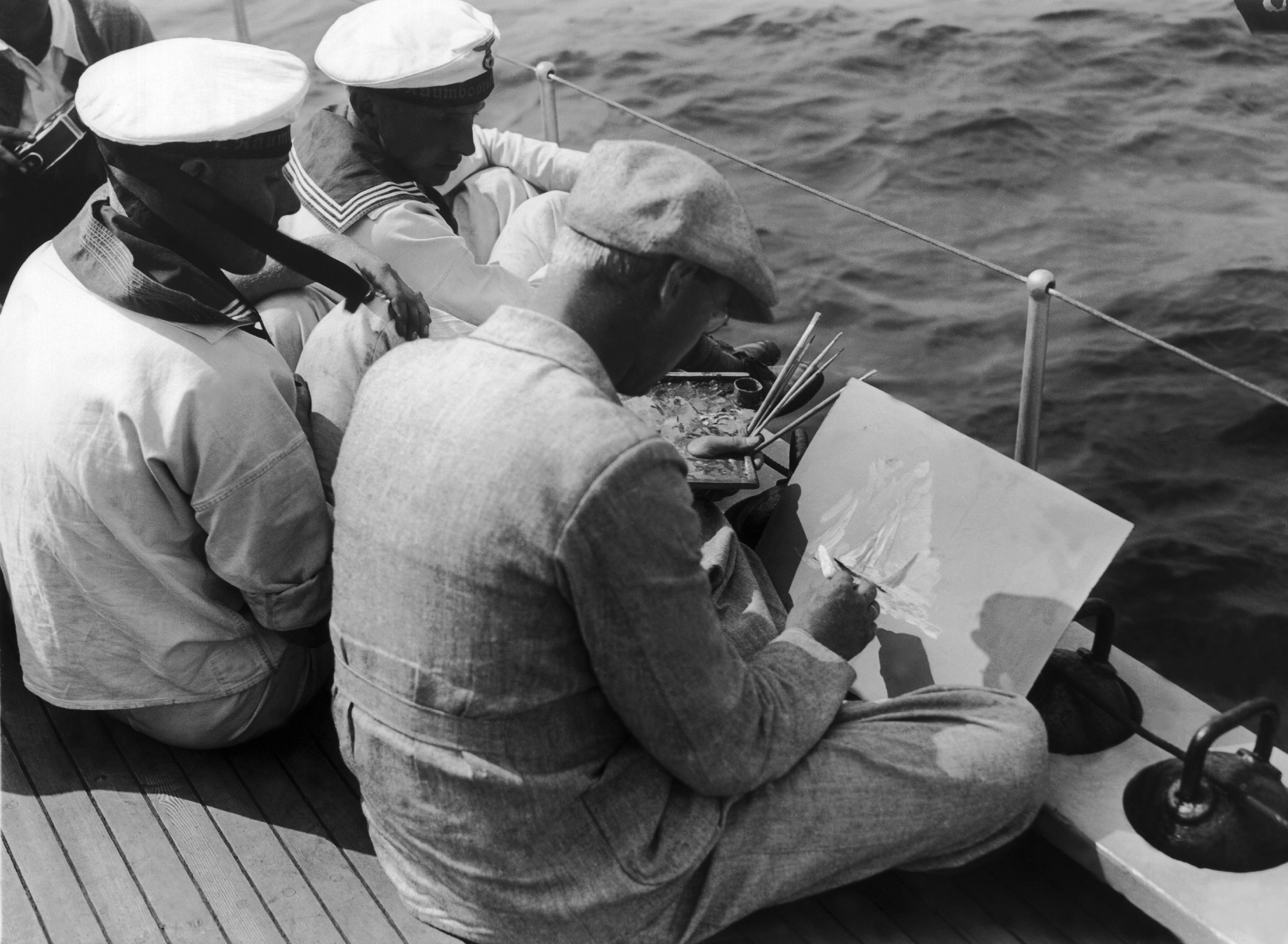 A man in a suit paints on a canvas while sitting on a boat deck, accompanied by sailors in uniform, with the ocean in view
