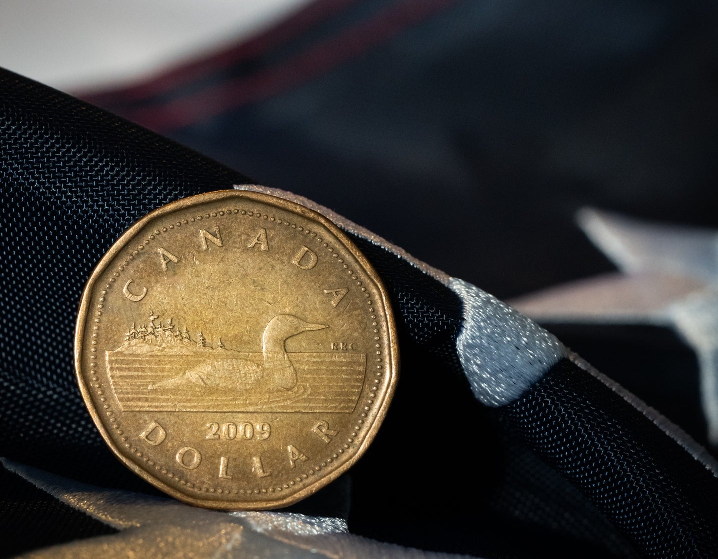 Canadian one-dollar coin on U.S. flag fabric, symbolizing economic relations between Canada and the United States