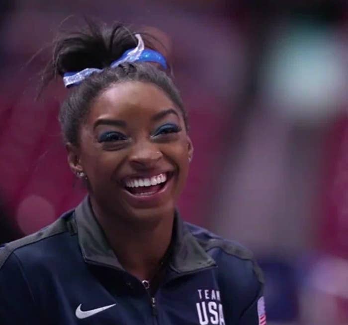 Gymnast in Team USA jacket smiling broadly with hair tied in a bun