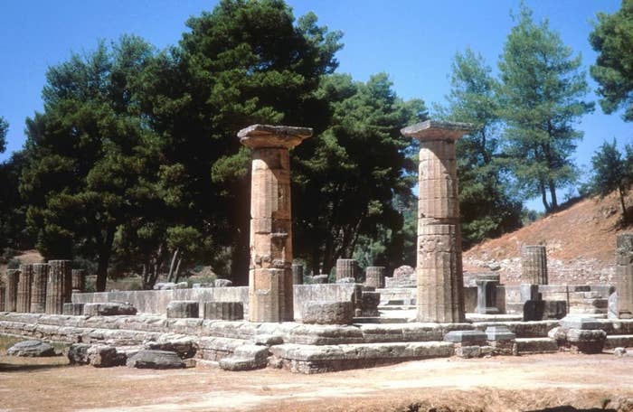 Ancient ruins with standing stone columns amidst a forested landscape, exemplifying historical architecture
