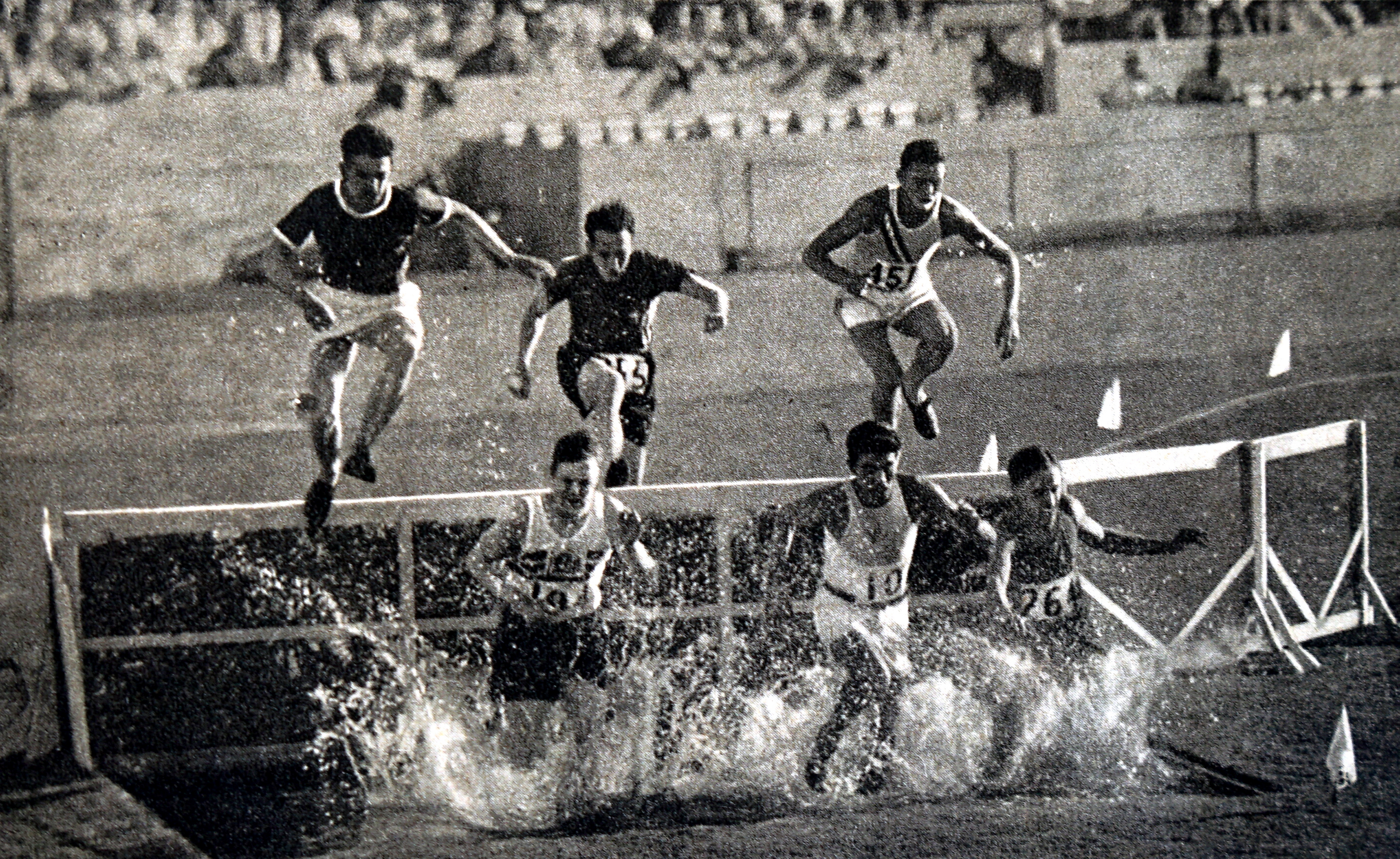 Vintage photo of athletes mid-air as they leap over a water barrier during a steeplechase race, with spectators in the background