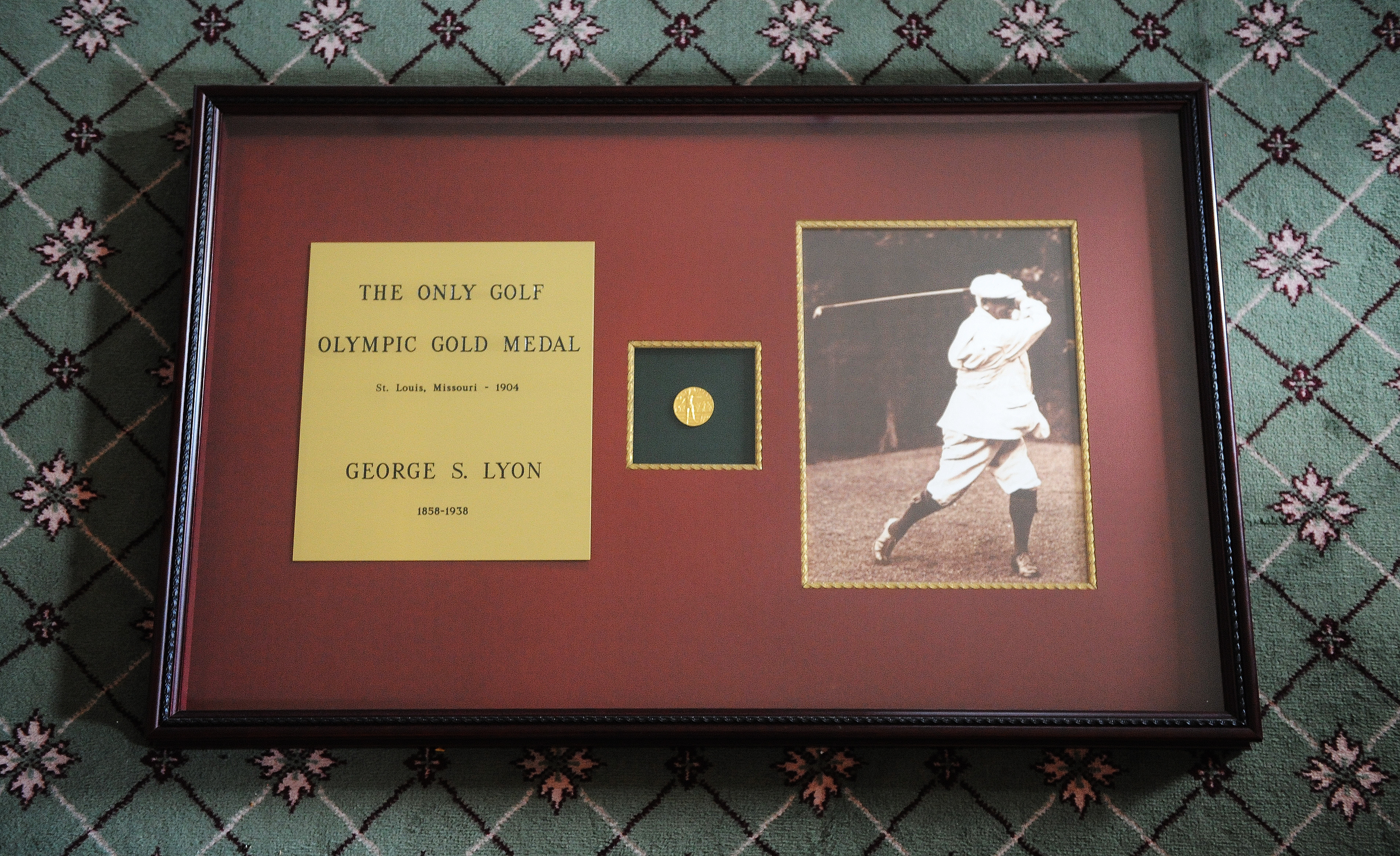 Framed display of George S. Lyon's 1904 Olympic golf gold medal with vintage swinging golfer photo and text detailing the achievement
