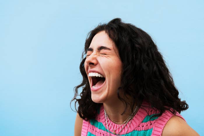 Person with curly hairsbreadth  laughing joyfully against a plain background, wearing a patterned sleeveless top
