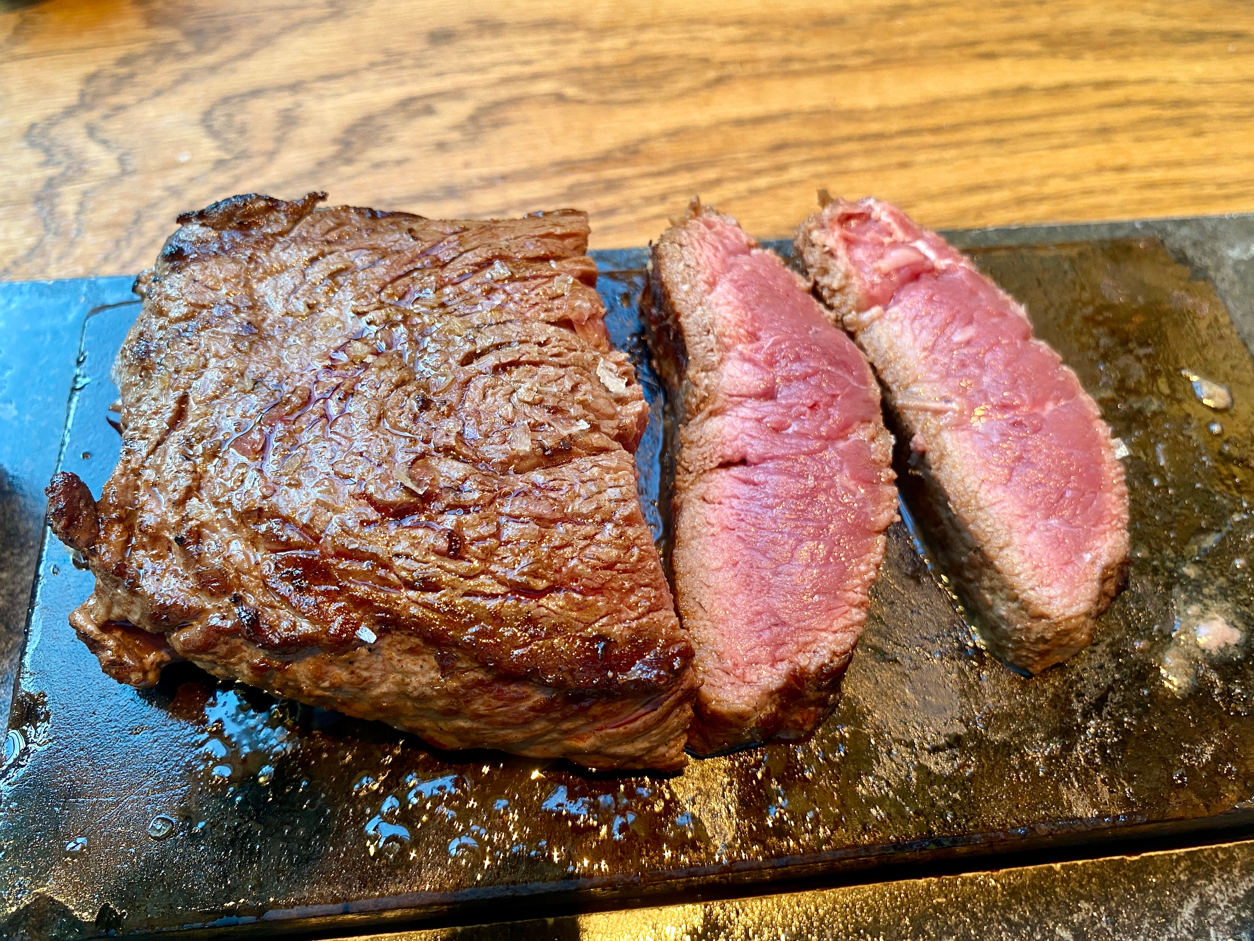 ステーキがカットされ、石板の上に置かれた様子。肉はジューシーで、焼き加減はレア。