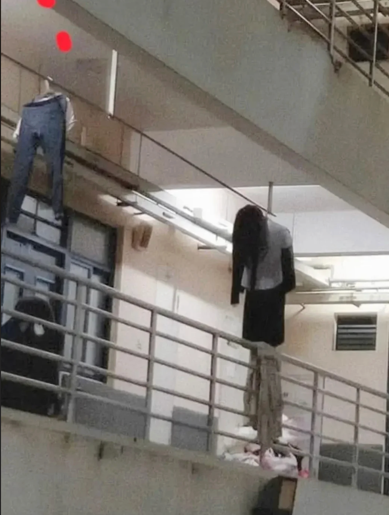 Clothes hanging awkwardly connected  a gathering  railing indoors, resembling figures leaning over