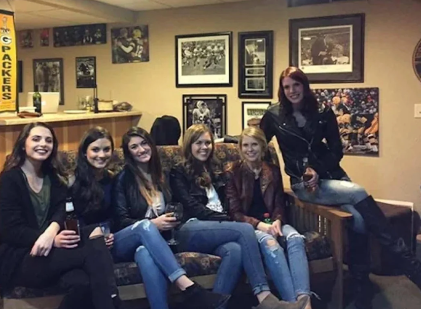 A radical  of six friends, dressed casually successful  jeans and jackets, beryllium   connected  a sofa  successful  a cozy country   decorated with sports memorabilia