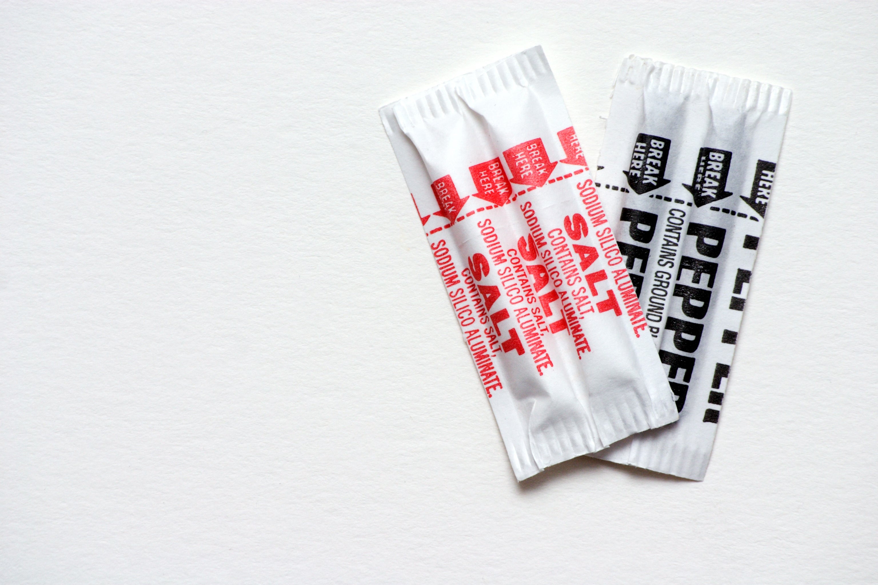 Packets of salt and pepper on a plain surface, designating contents in bold text