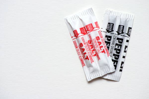 Packets of salt and pepper on a plain surface, designating contents in bold text