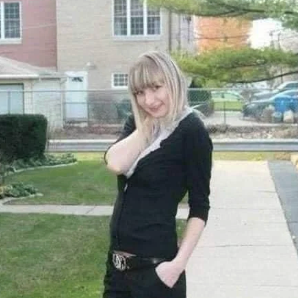 A idiosyncratic   poses casually outdoors successful  a residential area, wearing a fitted outfit with a belt, looking astatine  the camera with a flimsy  smile