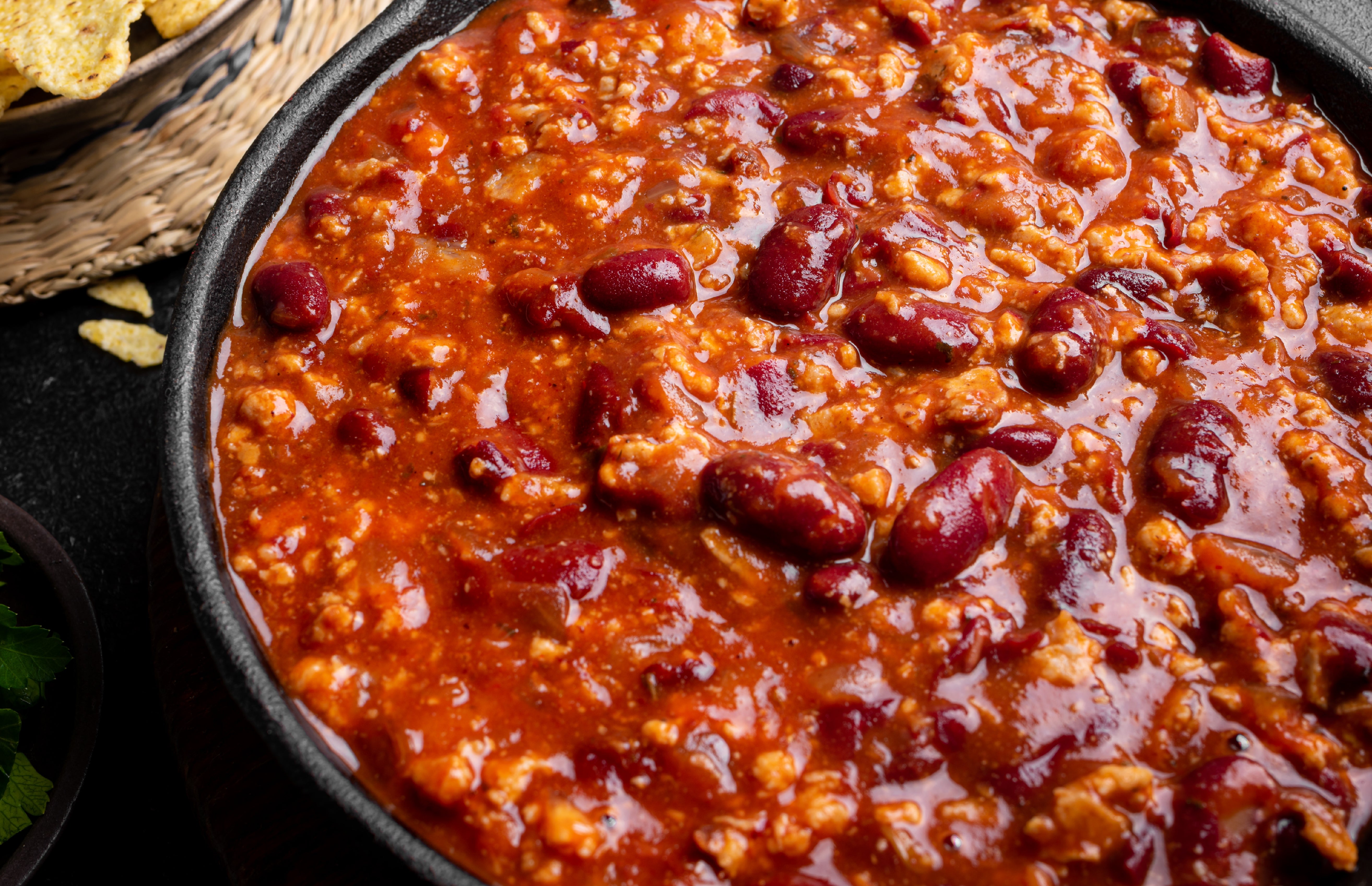 A bowl of chili with ground meat and kidney beans, served with tortilla chips nearby