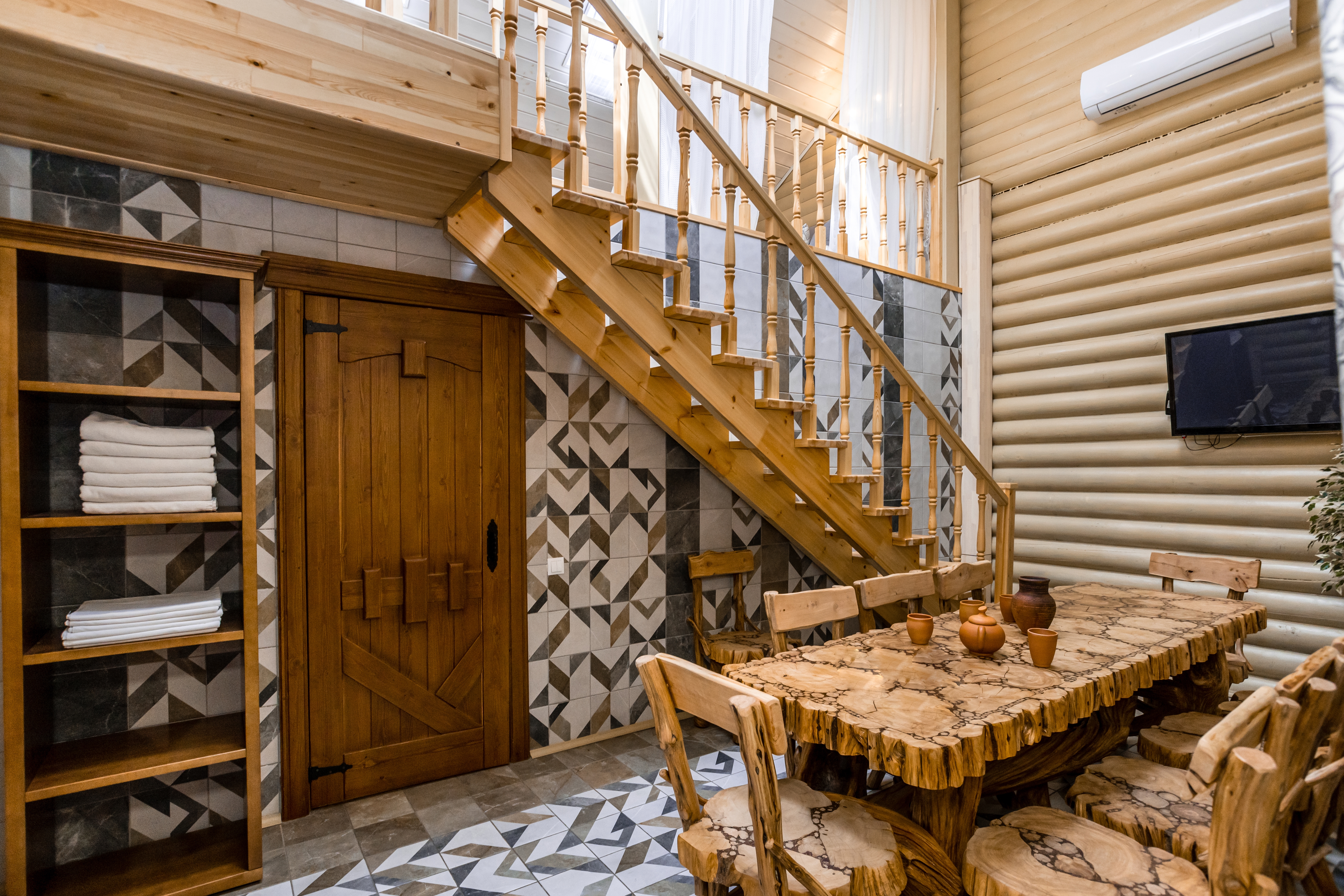 Rustic country   with a log staircase, geometric partition  tiles, woody  array  and chairs, towel shelf, and TV. Cozy and modern   interior design