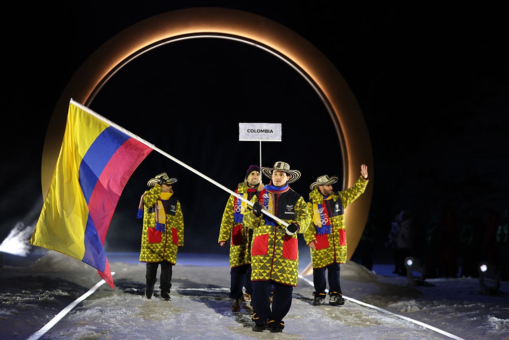 Colombia's team in traditional attire, holding a flag, parades under an arch at a sporting event