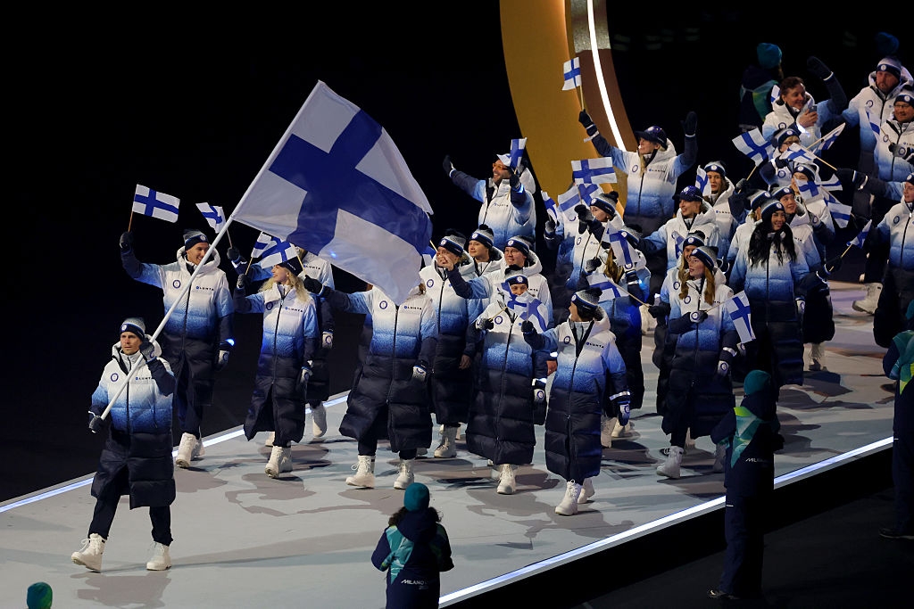 Team Finland enters a stadium during an event, wearing matching winter outfits and carrying national flags