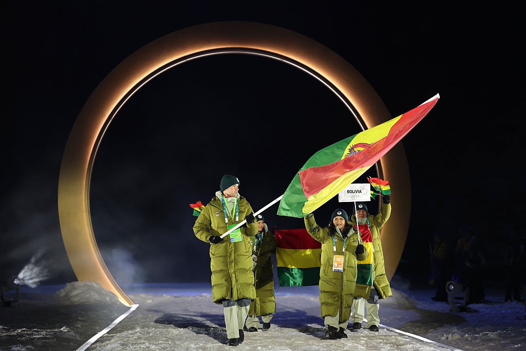 Individuals in warm coats carry flags during an outdoor ceremony