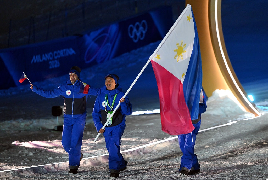 Athletes in blue outfits carry the Philippine flag during a Winter Olympics ceremony in a snowy setting