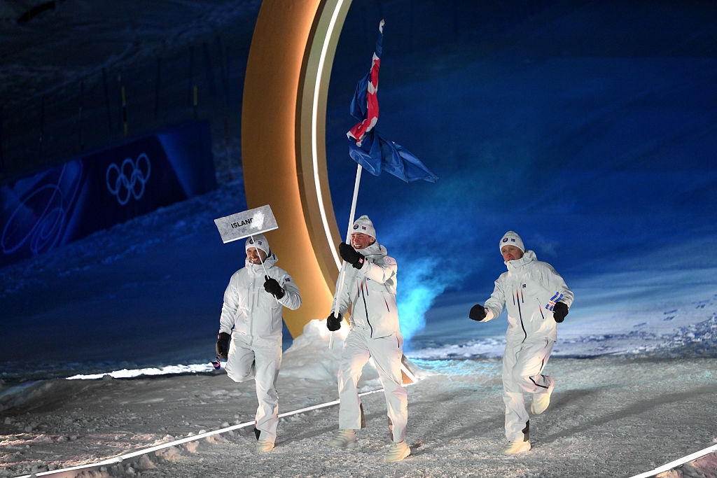 Athletes in white outfits march with the Icelandic flag at an Olympic event