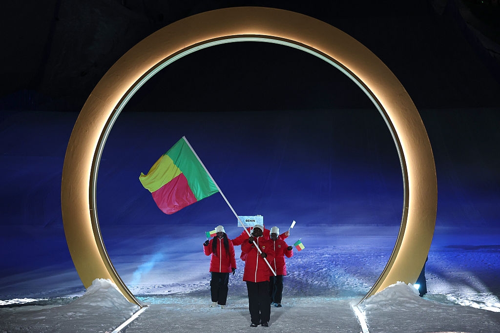 Individuals in red outfits carry a colorful flag through a large circular structure on a snowy surface at an event