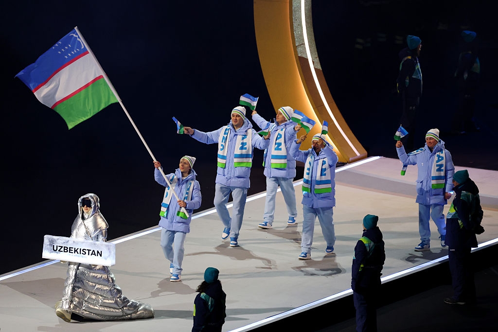 Athletes from Uzbekistan in matching winter outfits, waving flags, walk in a parade at a sports event
