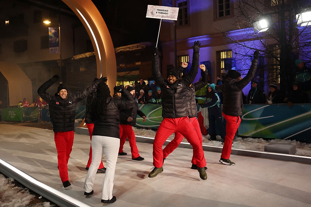 People in matching outfits, holding a "Trinidad and Tobago" sign, energetically celebrating at a winter event