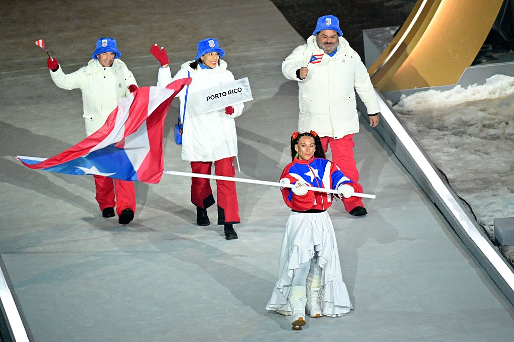 People in winter clothing are walking in a parade, one carrying the Puerto Rican flag and another holding a sign that says "Puerto Rico."
