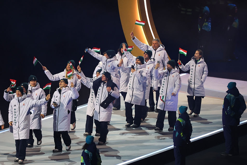 Group of athletes in white jackets waving flags during a sports ceremony
