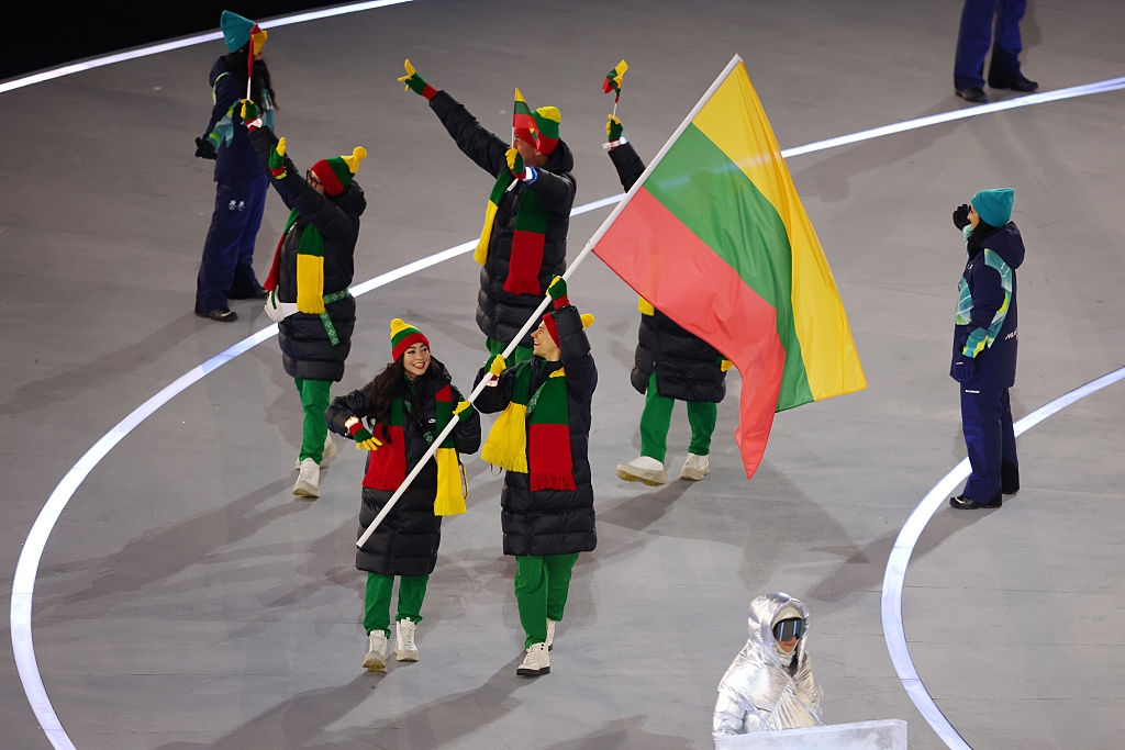 Group of athletes in winter gear, carrying a large flag at an indoor event, with vibrant scarves and hats
