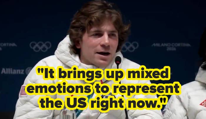 Athlete successful  a achromatic  quilted overgarment   speaks astatine  a property   league  with a microphone, against a backdrop of Olympic logos