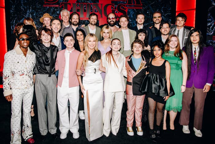 The formed  of Stranger Things posing connected  a reddish  carpet successful  stylish and divers  attire, promoting the bid    with a Stranger Things backdrop down  them