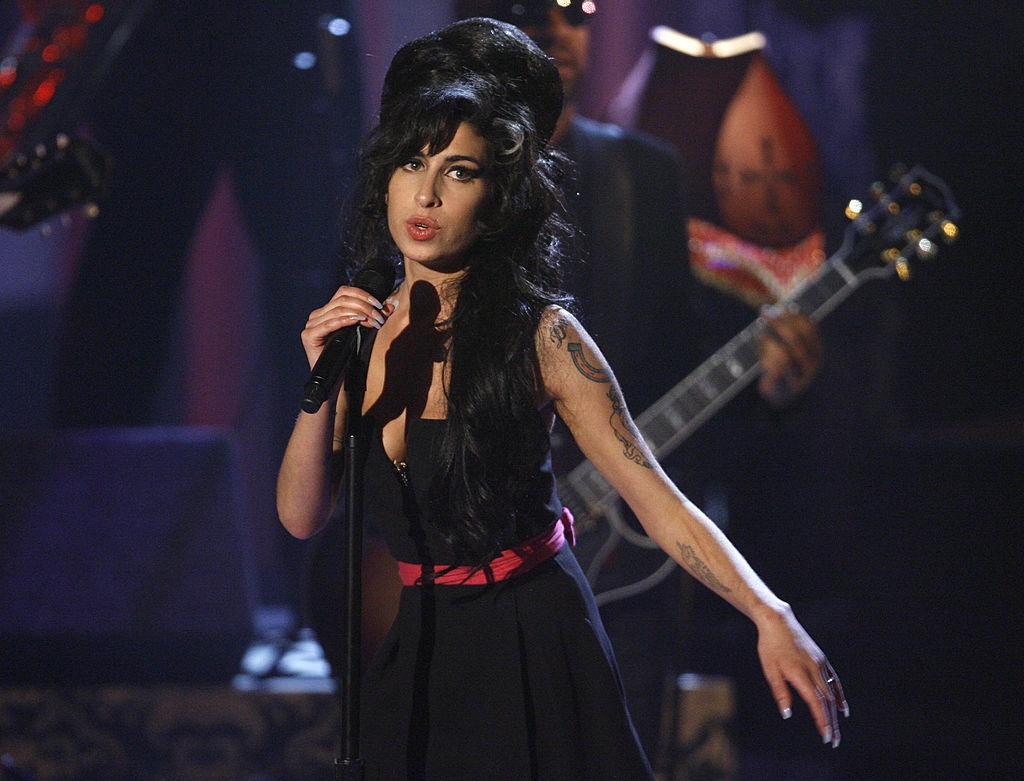 Singer performing connected signifier with a microphone, wearing a classical formal and styled hair. Guitarist disposable successful the background