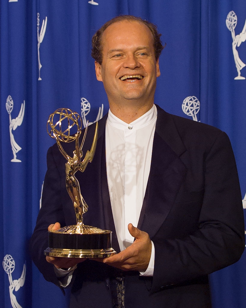 Person holding an Emmy award, dressed successful a classical achromatic tuxedo with a achromatic shirt, smiling astatine an grant event