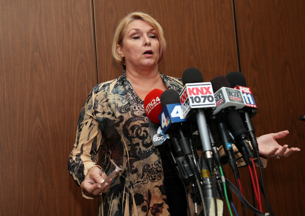 A idiosyncratic stands astatine a podium surrounded by microphones, speaking to the press. They are wearing a patterned outfit and holding a tiny object