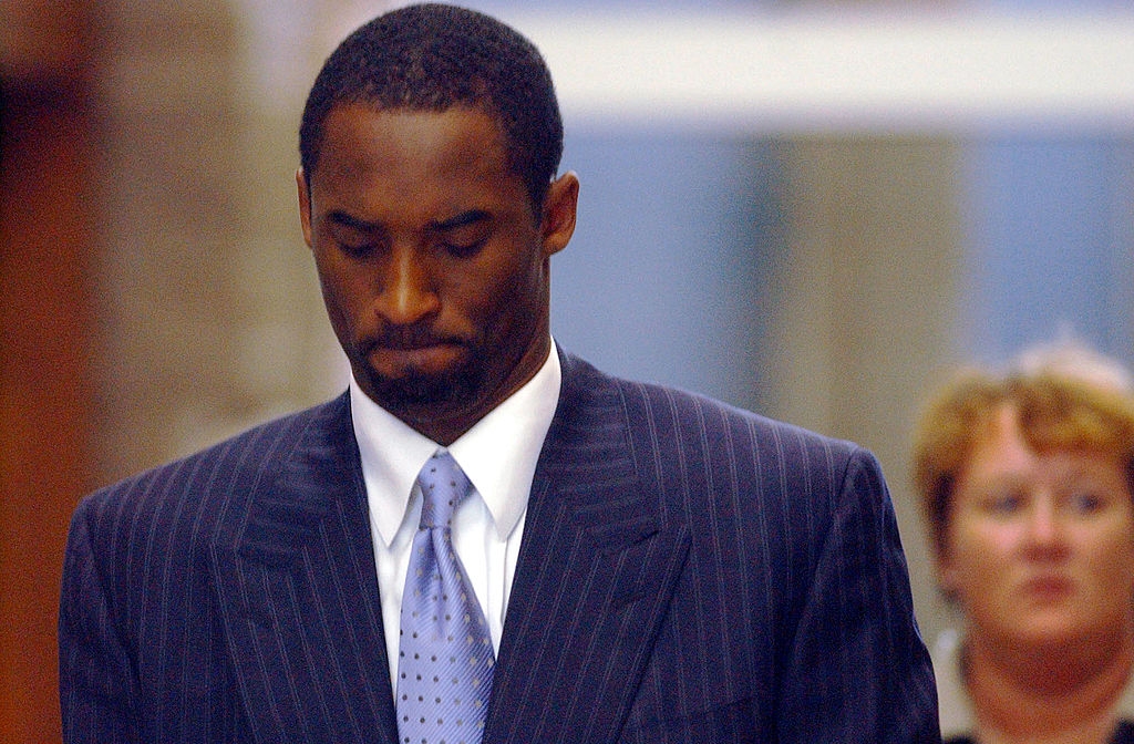 A idiosyncratic successful a pinstripe suit and necktie looks down with a thoughtful expression. Another idiosyncratic is blurred successful the background