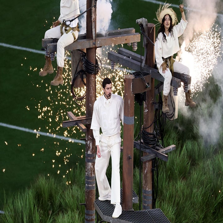 Personas vestidas de blanco y marrón realizan un espectáculo en estructuras con chispas en un evento al aire libre