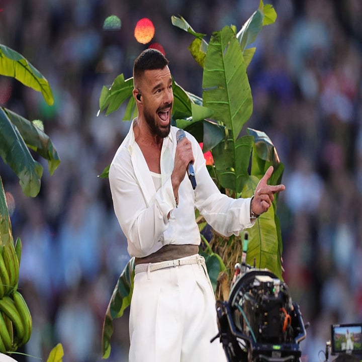 Cantante enérgico actuando en un escenario al aire libre, rodeado de plantas tropicales, con traje blanco elegante