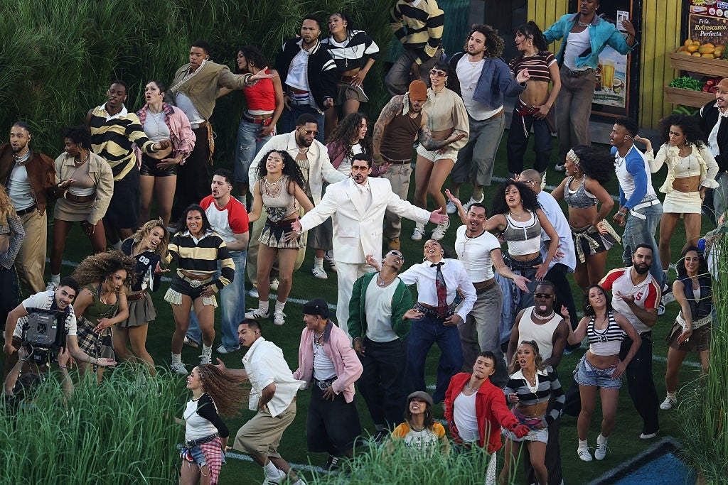 Grupo de personas en actuación enérgica al aire libre, con un individuo en el centro vistiendo un traje blanco. Varios estilos de ropa casual