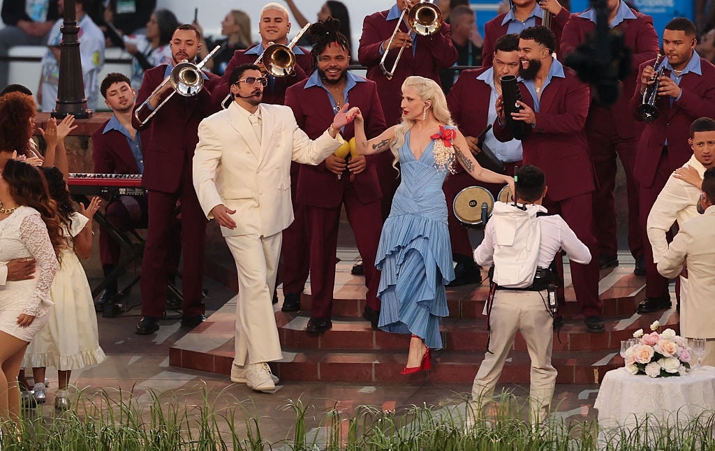 Un grupo musical acompaña a una pareja bailando; el hombre lleva traje claro y la mujer un vestido largo con volantes. Hay público alrededor