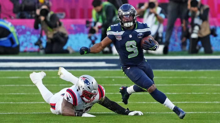Jugador de fútbol americano con uniforme Seattle Seahawks evade a un oponente de los Patriots en el campo durante un partido