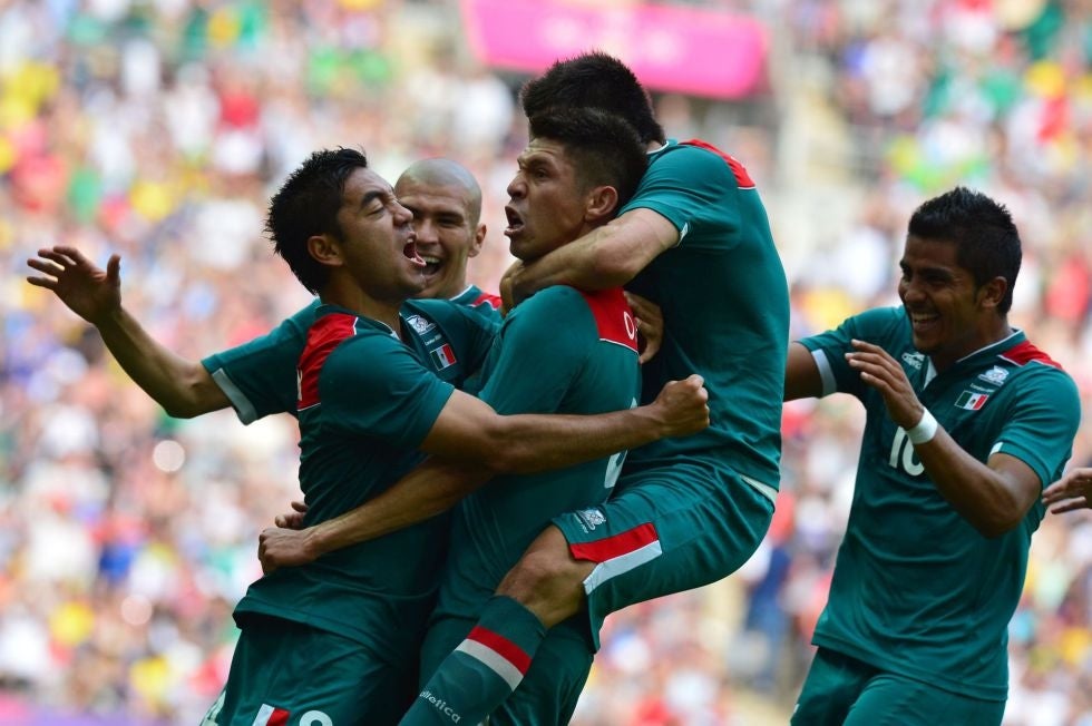 Jugadores de fútbol celebran un gol en un partido, abrazándose y mostrando emoción en el campo. Están vestidos con uniformes deportivos