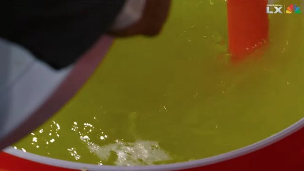 Persona moviendo un líquido amarillo en un gran recipiente. No se presenta contexto adicional