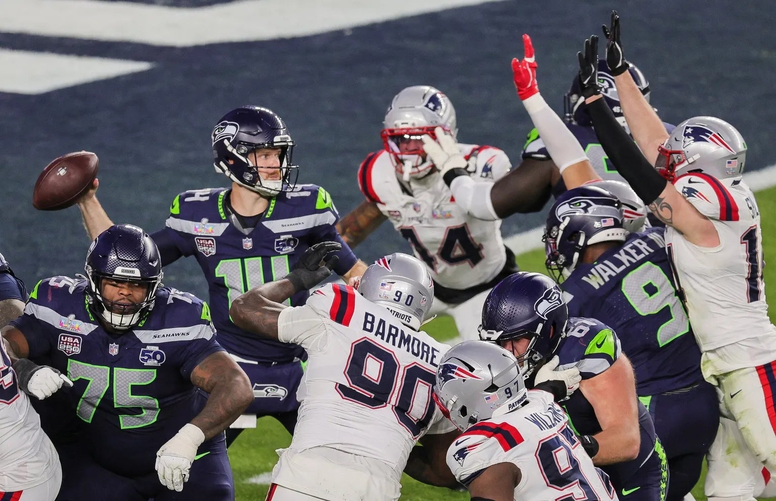 Jugadores de fútbol americano del equipo Seahawks y Patriots en acción durante un partido, con un campo de juego y balones visibles