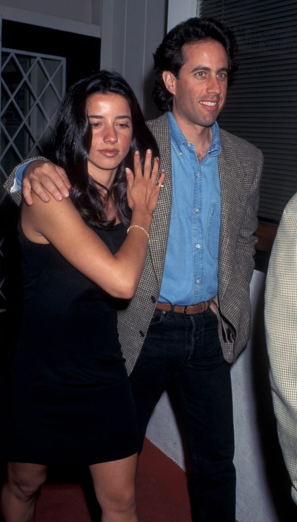 A well-dressed mates poses together, 1 wearing a casual blazer and jeans, and the different successful a stylish sleeveless dress