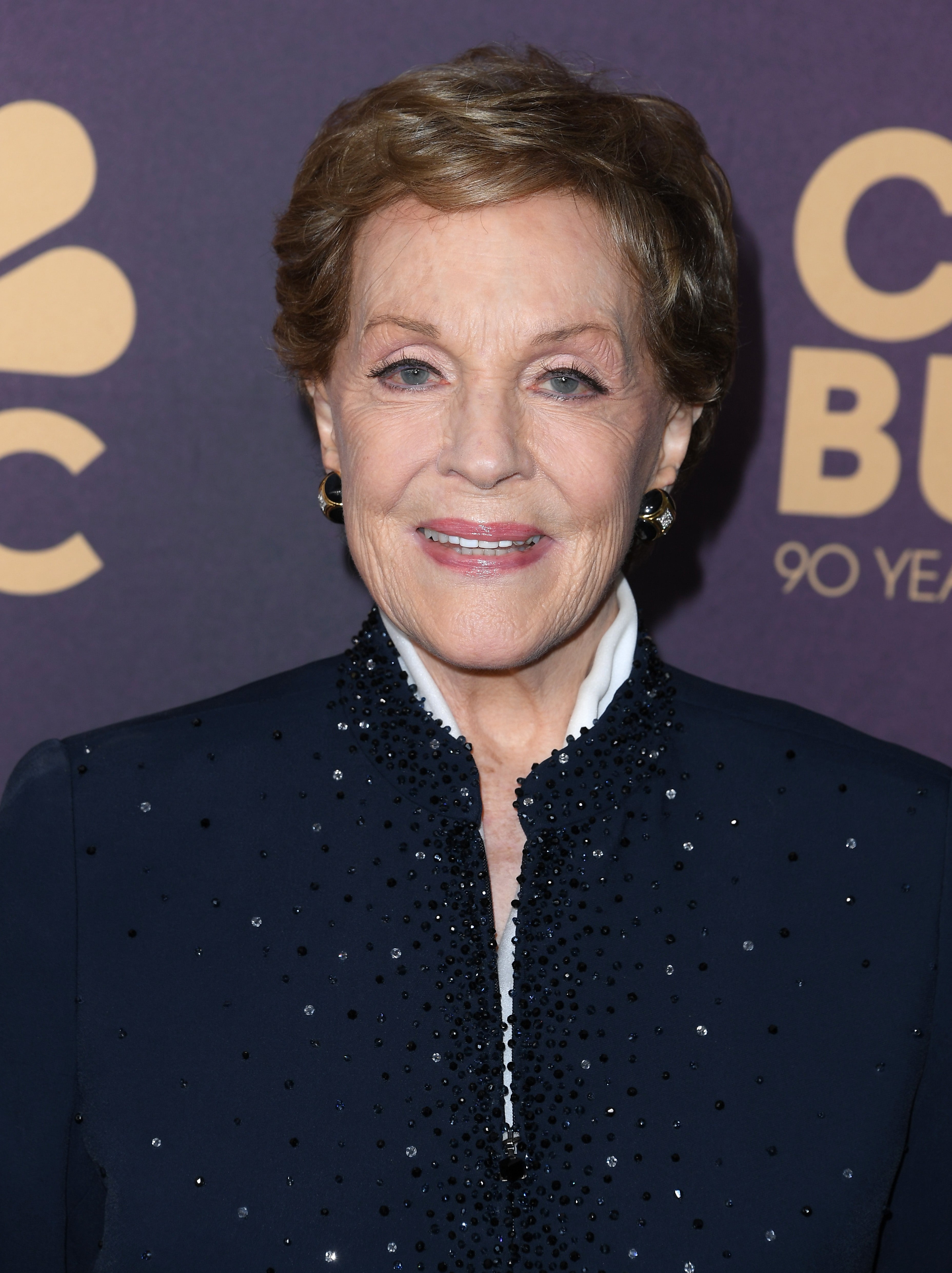 Person smiling at an event, wearing an elegant, embellished jacket