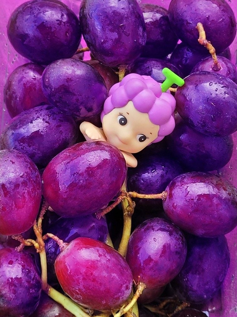 Muñeco con cabello de uva entre varias uvas reales
