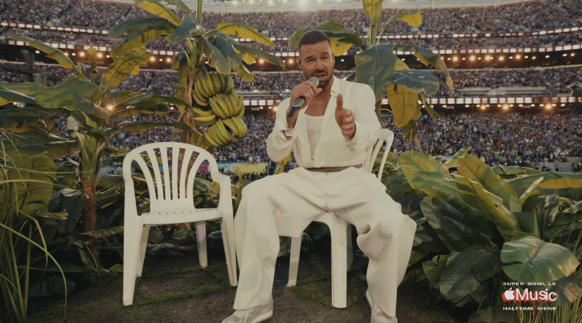A idiosyncratic   successful  a achromatic  suit   performs portion    seated connected  a signifier    surrounded by plants, with a ample  assemblage  successful  the stadium seats down  them