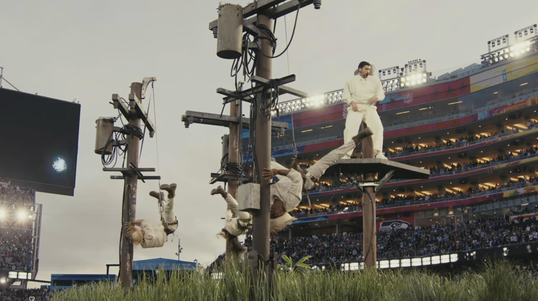 Performer lasting  connected  level    during a stadium performance  with dancers hanging from poles, creating a dynamic ocular  show
