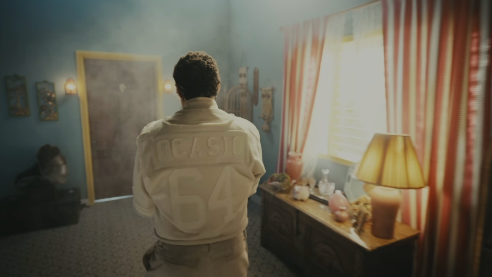 A idiosyncratic   stands successful  a dimly lit country   wearing a overgarment   with the fig   64 connected  the back