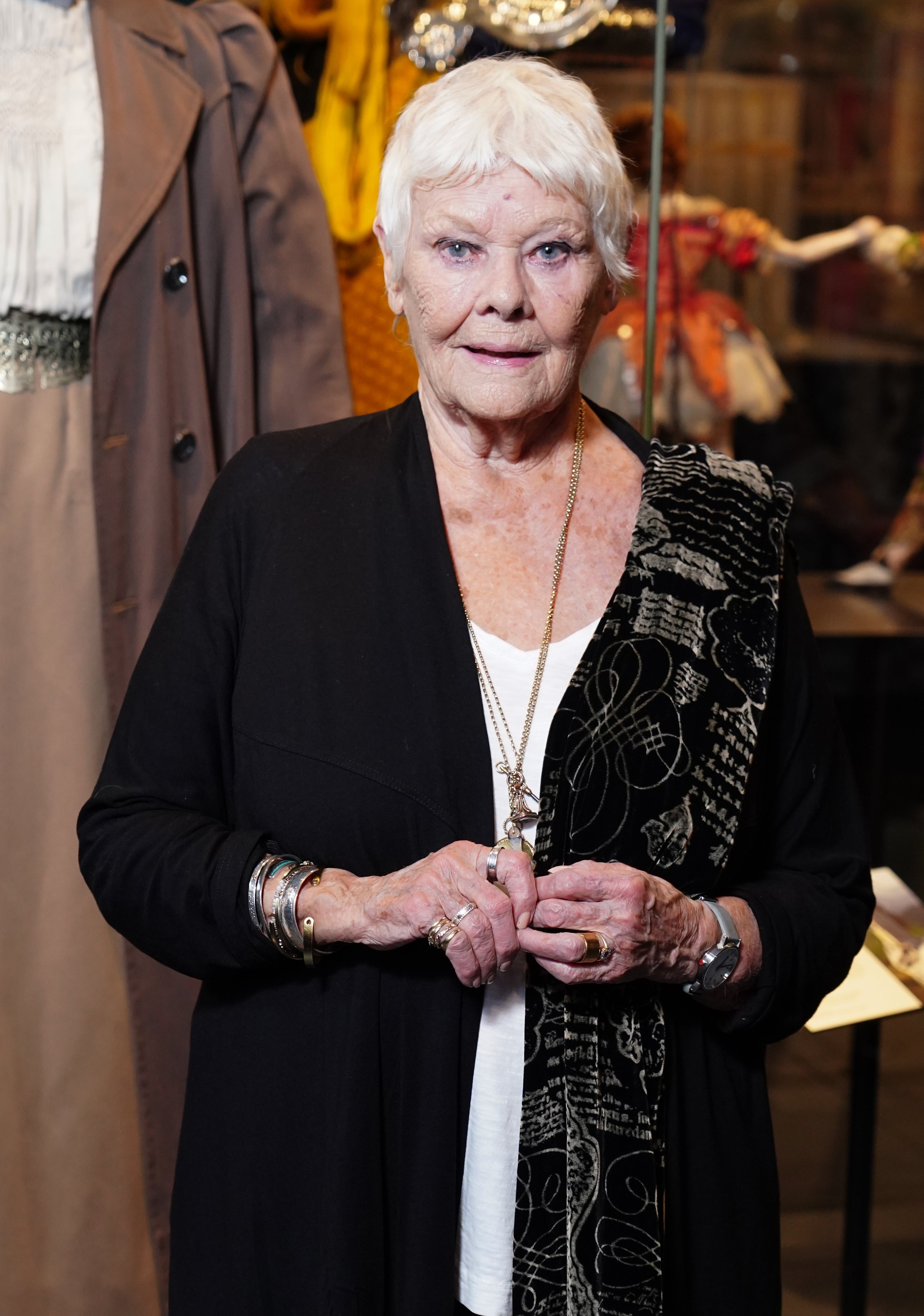Person wearing a black and white patterned shawl over a black outfit, standing in front of a display with vintage clothing